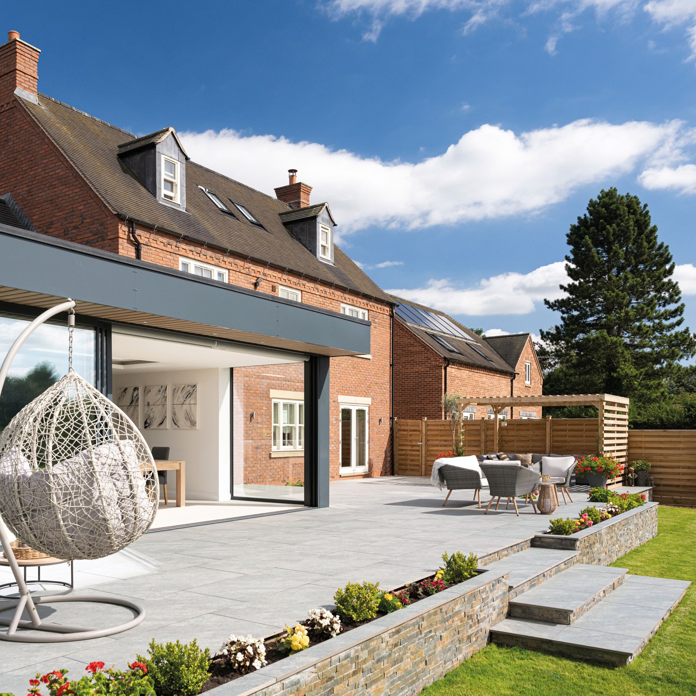Pale porcelain paving connecting a garden terrace to a brick home